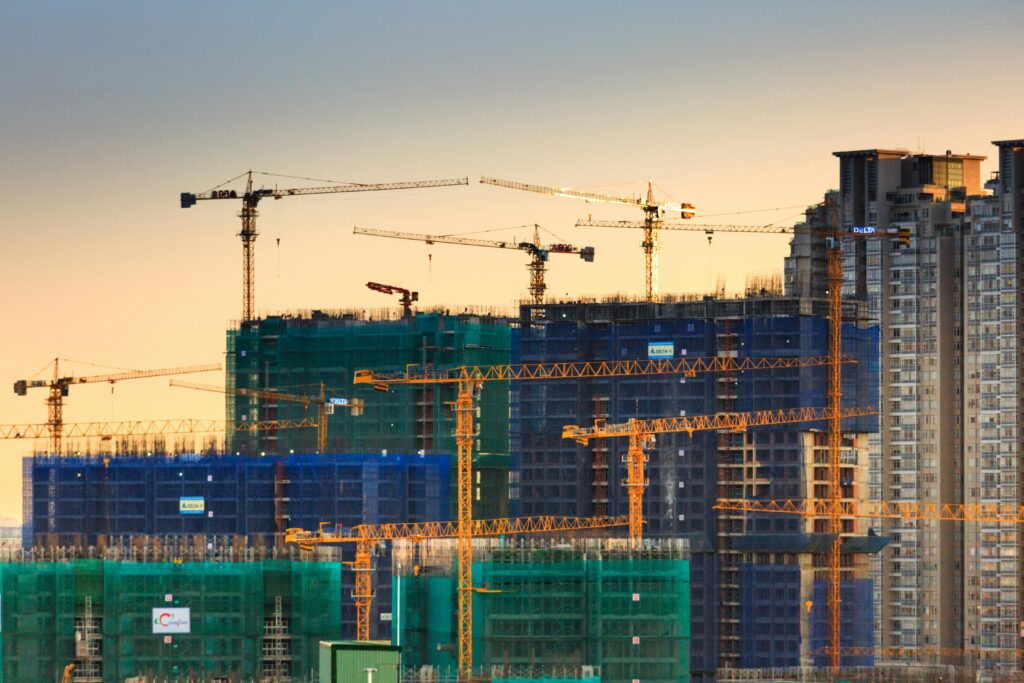 Services A cityscape featuring high-rise buildings under construction with cranes during sunset.